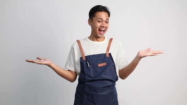 A young man wearing an apron opened his hands to the right and left at the empty space with a surprised expression.