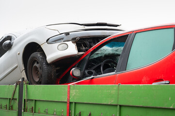 Damaged crashed vehicle after car accident collision, broken window, cars inside a towing trailer driving to a junkyard 
