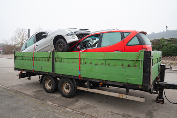 Damaged crashed vehicle after car accident collision, broken window, cars inside a towing trailer driving to a junkyard 