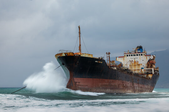 View of the stranded rusting ship battered by crashing waves under a gloomy sky, a stark contrast against the sandy beach, Delisha Beach, Socotra, Yemen.