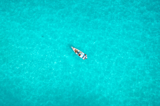 Aerial view of a small boat drifting on the turquoise waters, the sun reflecting off the ripples creating a shimmering effect, Kalleesa, Yemen.