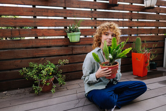 Woman sitting and holding potted plant on terrace