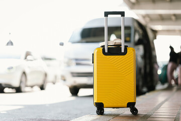 A bright yellow rolling suitcase stands at a transport pickup area with vehicles in the background, symbolizing arrival, departure, and modern urban travel lifestyle. © Worawi