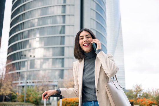Businesswoman walking with suitcase and talking on mobile phone outdoors