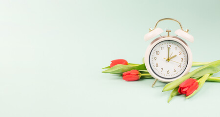 Switch to daylight saving time in spring, summertime changeover, alarm clock with red tulip flowers
