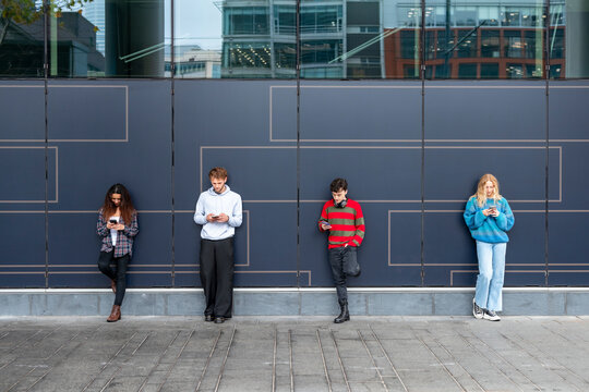 Young adults standing outdoors using mobile phones in urban setting