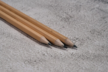 Three natural wooden pencils lie side by side on a mottled light gray background