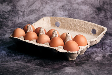 Ten warm brown eggs in an open eco-pulp carton reflect light on a dark surface, hinting at culinary use