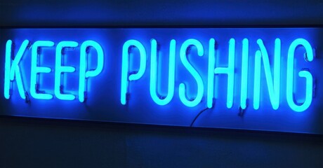 Fototapeta premium Bright blue neon sign displays motivational phrase. Dark background emphasizes glowing text, simple design.