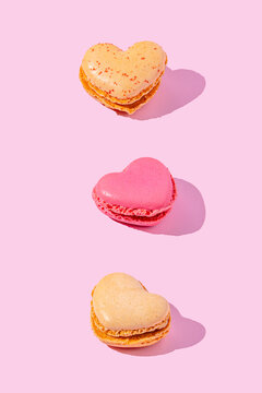 Heart shaped pink macarons arranged in a vertical pattern on pink