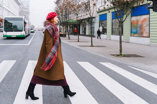 Woman in overcoat and scarf walking on city crosswalk