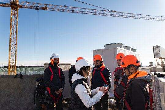 Female engineer leading discussion with construction workers on rooftop job site