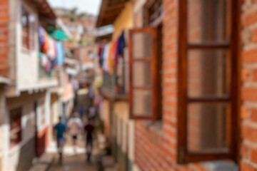 Obraz premium Blurry image of people walk through a narrow alley lined with shops and residential buildings, reflecting the vibrant and bustling local life