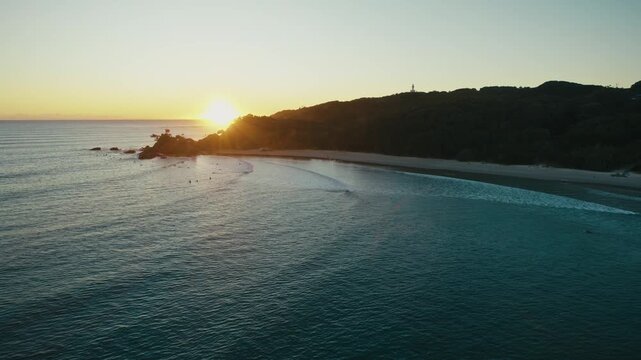 Sunlit headland and smooth surf define Byron Bay coast in early daylight