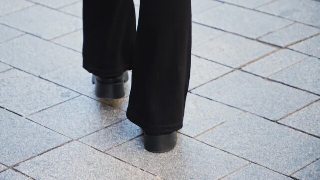 A rear view of legs walking on asphalt legs in black boots, close-up.