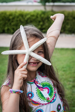 Portrait of a smiling girl with a missing tooth holding a starfish in front of her face