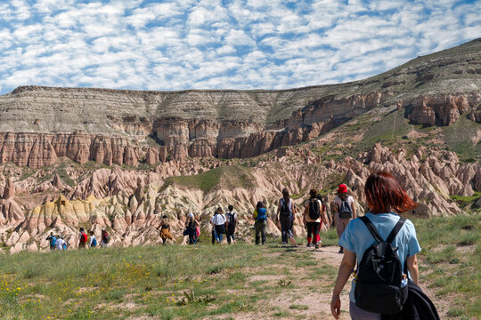 Rear view of a large group of hikers walking in a single line towards massive layered rock formations in Cappadocia, Turkey