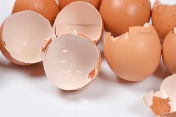 A close up side view of several empty and broken brown eggshells resting on a plain white surface after being used for cooking