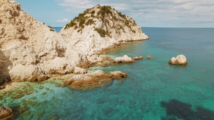 Rocky coastline with turquoise sea and rugged cliffs under bright sky in Greece.