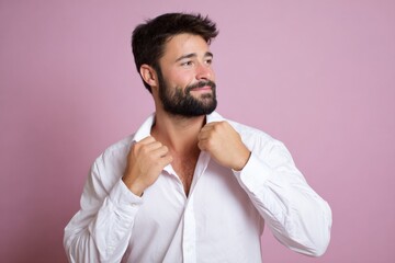 Obraz premium Young caucasian male adjusting white shirt against pink background