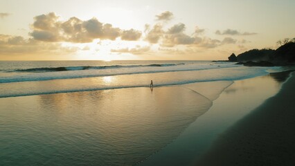 Woman with long hair walking on water during sunset on reflective Ostional beach in Costa Rica.