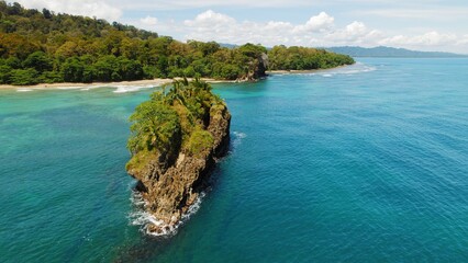 Obraz premium Rocky palm covered islet off lush tropical Caribbean coastline in Costa Rica.
