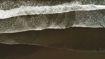 Abstract aerial lines of ocean waves on dark sand beach in Costa Rica at overcast dusk. © Olga Gorkun
