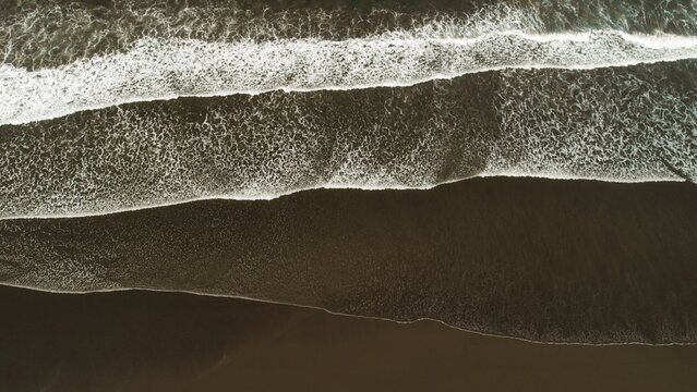 Abstract aerial lines of ocean waves on dark sand beach in Costa Rica at overcast dusk.