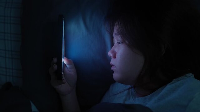 Asian woman lying in bed scrolling on her smartphone before bedtime, enjoying short-form video content on a digital platform