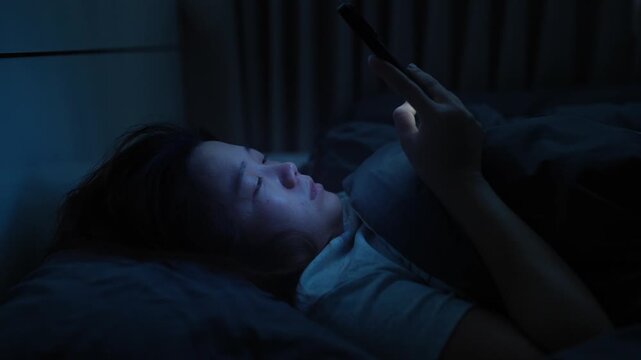 Asian woman lying in bed scrolling on her smartphone before bedtime, enjoying short-form video content on a digital platform