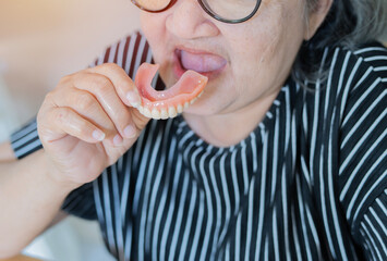 An old gray-haired woman puts on her denture. The senior woman holds the denture.