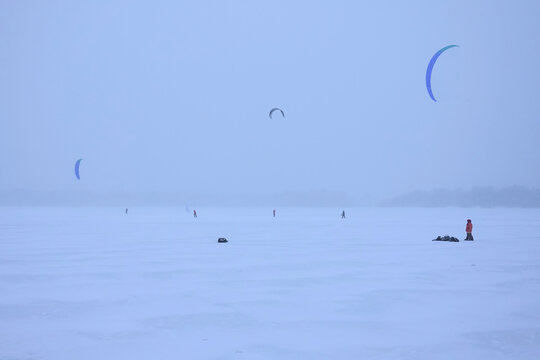 Snowkite sportsmens have training on a vast frozen lake surface in winter in blizzard overcast day