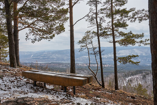 Wooden bench on a snowy hill overlooking a panoramic mountain landscape. Outdoor relaxation in a winter forest setting