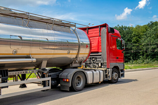 A large red truck with a silver tanker trailer on a road..