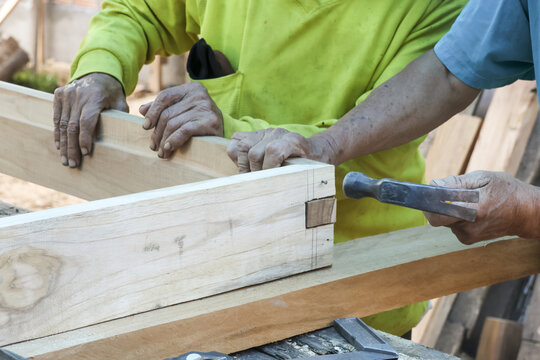 Skilled carpenters focusing on assembling wooden frame with hammer in workshop showing hardworking spirit and precise craftsmanship during construction process