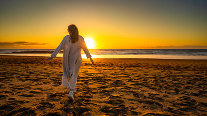 Beautiful middle-aged woman enjoying walk on sandy beach on sunset on windy spring day. Back view
