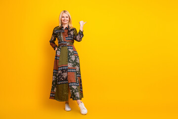 Elegant mature woman in patchwork dress smiles and poses against a bright yellow background suitable for fashion lifestyle and advertising