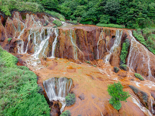 Aerial close-up of Golden Waterfall near Jiufen, Taiwan, highlighting rust-colored mineral rocks and flowing water, revealing striking textures, erosion patterns, and vivid natural colors.

