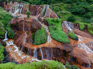 Aerial view of the Golden Waterfall near Jiufen, Taiwan, with mineral-rich water flowing over colorful rock formations, creating striking golden and orange tones in a rugged landscape.

