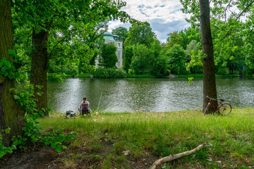 Woman Fishing on Banks of Spree River Berlin with Historic Belvedere Charlottenburg Palace and Lush Summer Greenery in Background