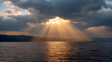 Dramatic sunbeams pierce through dark clouds over a vast lake casting golden light and reflections at dusk