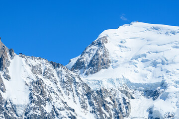 Naklejka premium Close-up view of the Mont Blanc massif reveals rugged rock faces and pristine snowfields under a vivid blue sky, with dramatic glacier formations cascading down the slopes.
