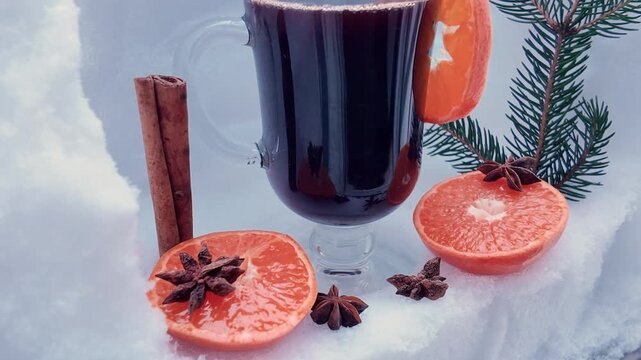 Mulled wine in a transparent glass mug, orange, spices against a snowy backdrop, winter composition.