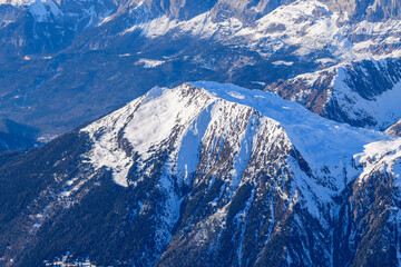 Fototapeta premium High angle view of the Aiguillette des Houches showing a broad snow-covered plateau bordered by steep forested slopes and deep valleys, illuminated by crisp winter sunlight.