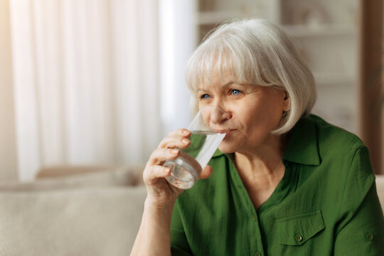 Senior caucasian woman drinking water at home, elderly female staying hydrated and healthy, simple retirement lifestyle and daily wellness routine indoors