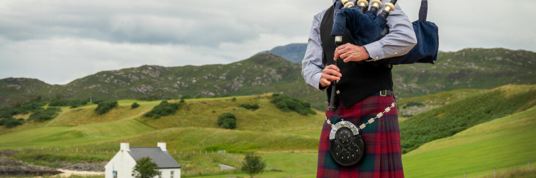 Scottish bagpiper in the Highlands of Scotland, panoramic mountains landscape background, UK