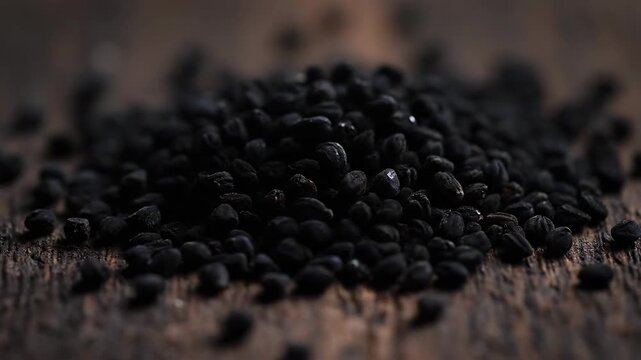 Pile of black cumin seeds on rustic wooden surface for culinary use, spice.
