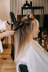 Naklejka premium Hair care. Blow drying with a special round comb for women's blonde-coloured hair in a beauty salon. Vertical image.