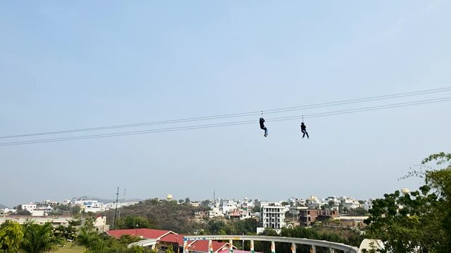 Two people ziplining over a cityscape in India