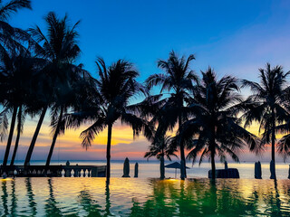 Obraz premium Stunning Sunset at Luxury Beach Resort with Infinity Pool, Silhouetted Palm Trees and Vibrant Twilight Sky in Vietnam